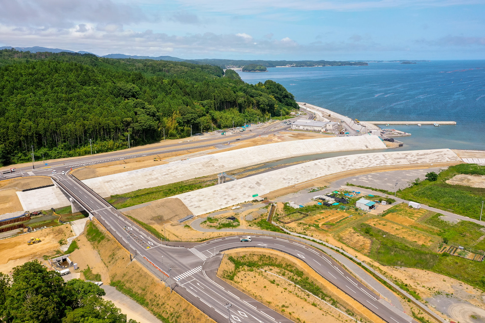 海岸沿いに道路と防波堤が伸び、周囲に海と空が広がる風景を空から見下ろした写真