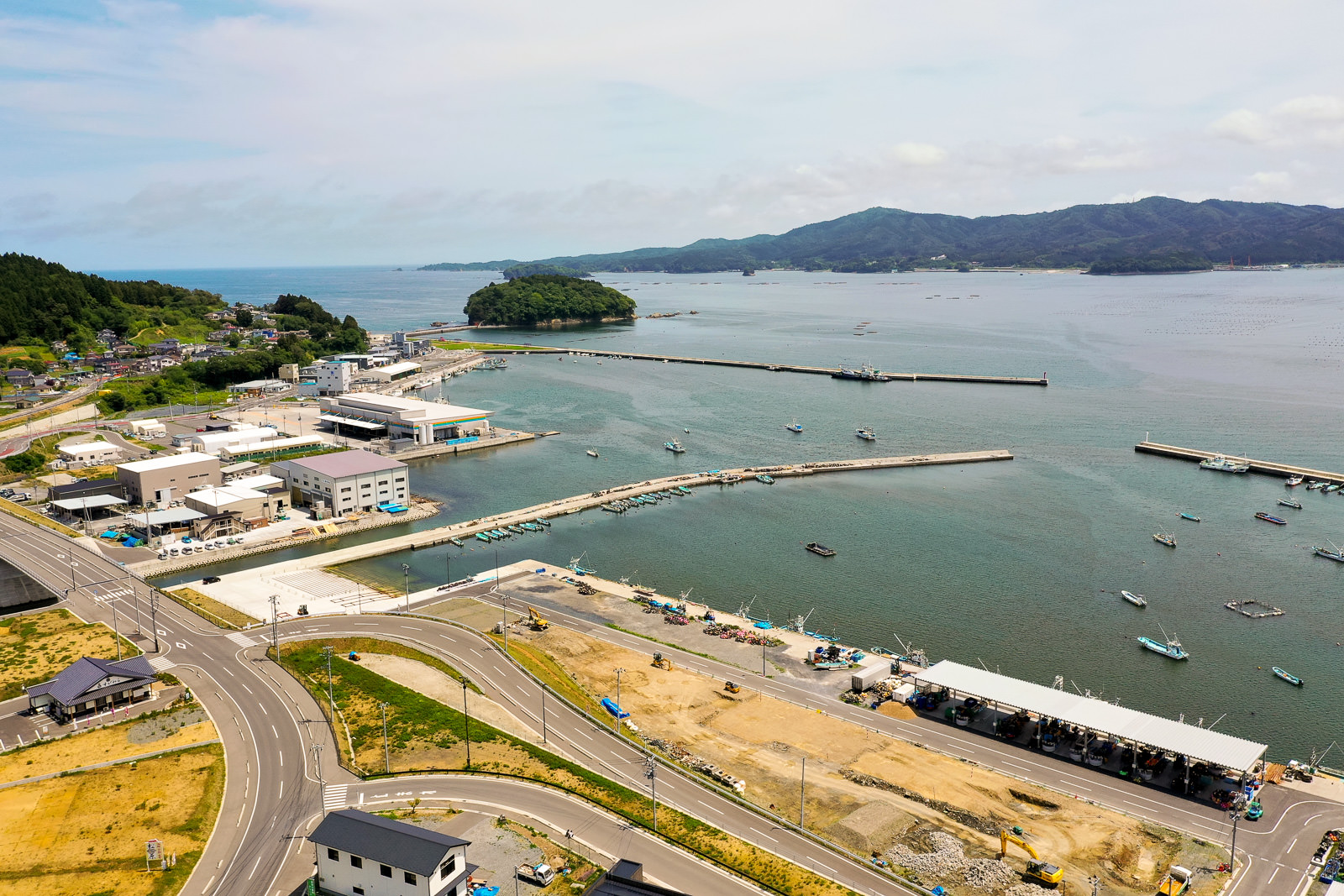 海に面した港町を空から見下ろし、複数の建物や道路が広がり、海には船が浮かぶ風景の写真