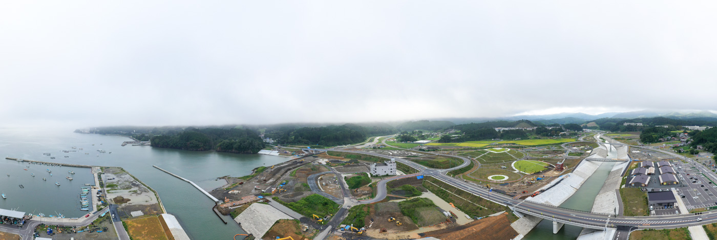 海岸沿いの町を上空から撮影した風景で、左側には港が広がり複数の船が停泊しており、右側には道路が網の目のように走り、その周囲に建物が密集して並んでいる海岸沿いの町の写真
