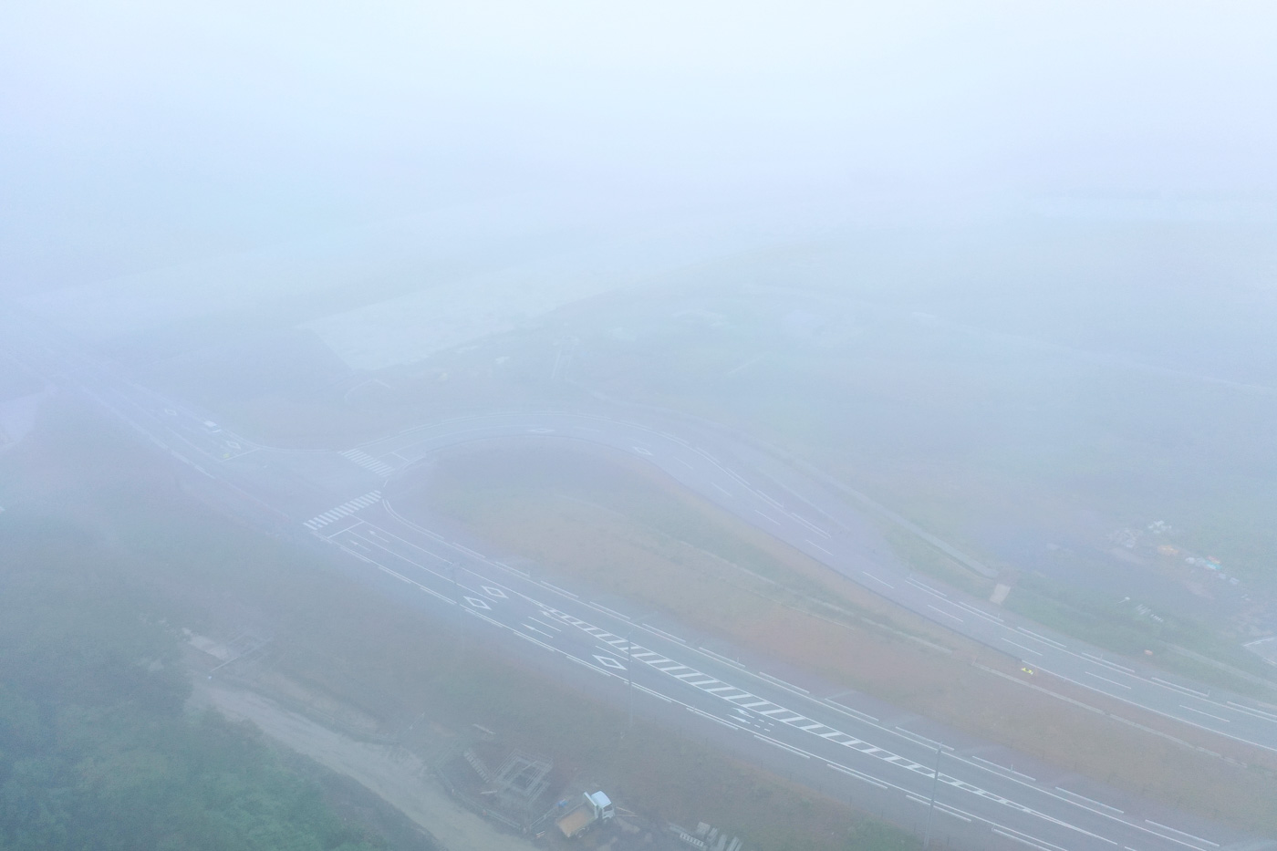 霧が濃く立ち込める中、舗装された道路が静かに伸びており、周囲の景色が白くかすんで見える幻想的な雰囲気の道路の写真