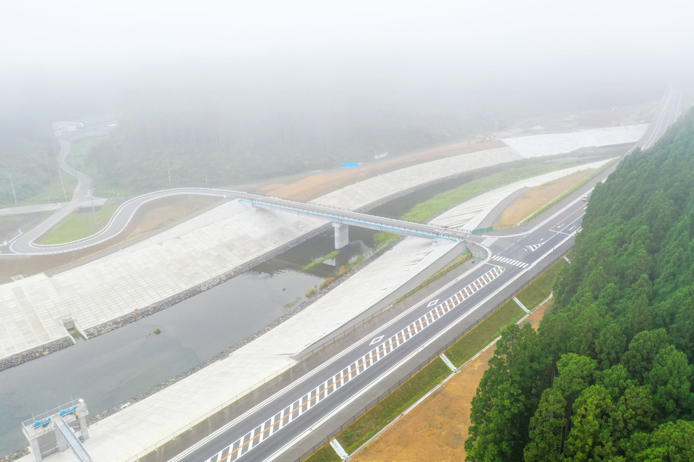 霧が立ち込める中、川と道路が交差する地点に架けられた橋の構造と周囲の風景を写した橋の写真