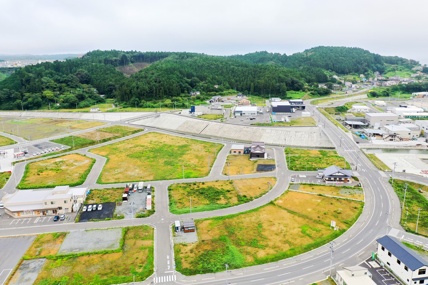 緑に覆われた丘に囲まれた広々とした空き地の中で、複数の舗装道路が交差しており、周囲には自然の地形が広がっている静かな郊外の風景の写真