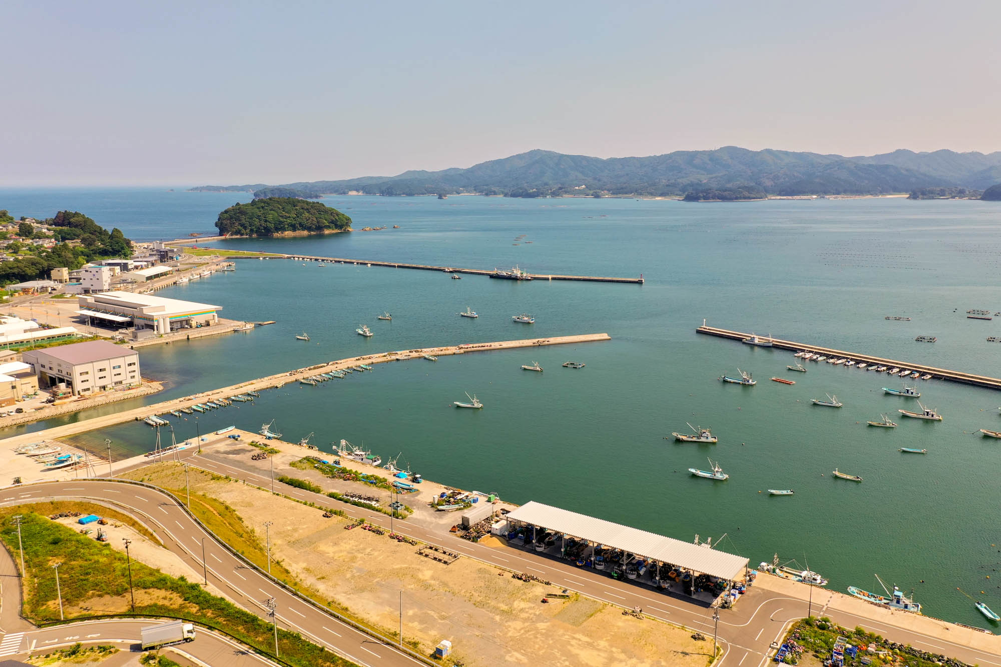 穏やかな海に面した南三陸町の港の風景で、漁船が停泊し、岸壁沿いに水産加工施設や建物が並んでいる写真