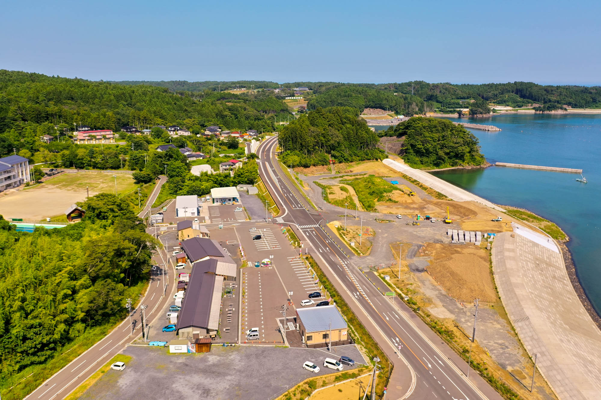 緑豊かな丘陵地帯に沿って海岸線が広がり、その周囲に道路や駐車場、建物が点在している自然と人の営みが調和した風景の写真