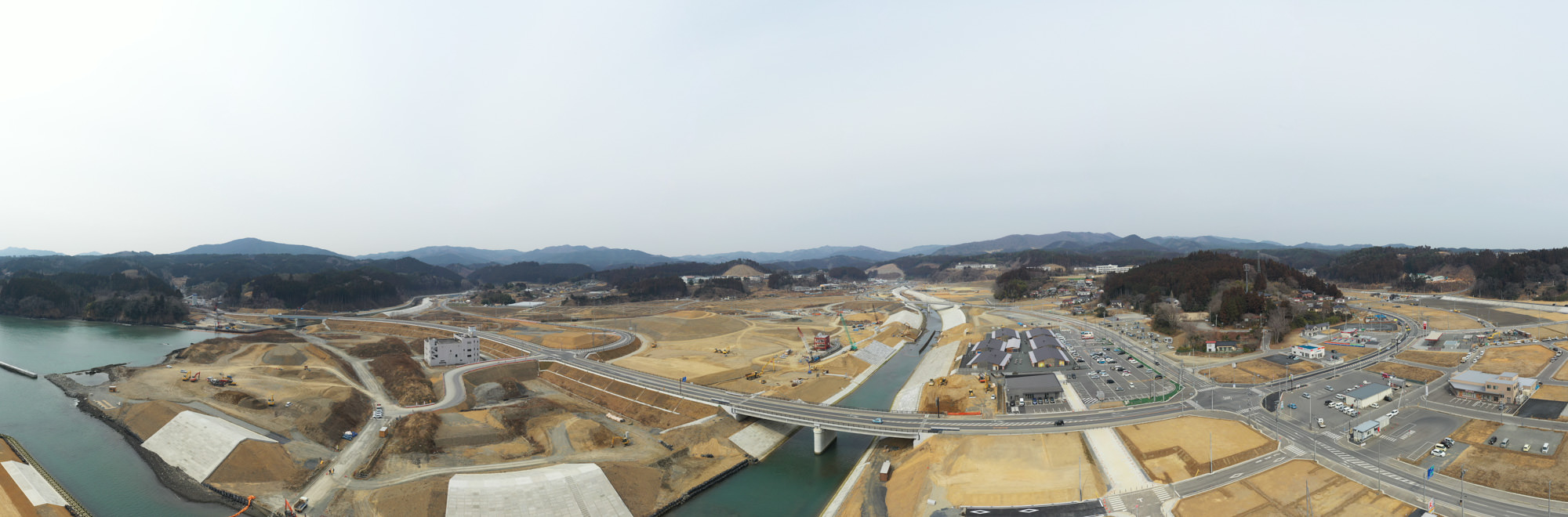 川を挟んで広がる広大な工事現場で、橋や道路が建設されている様子を上空から捉えた工事現場の写真