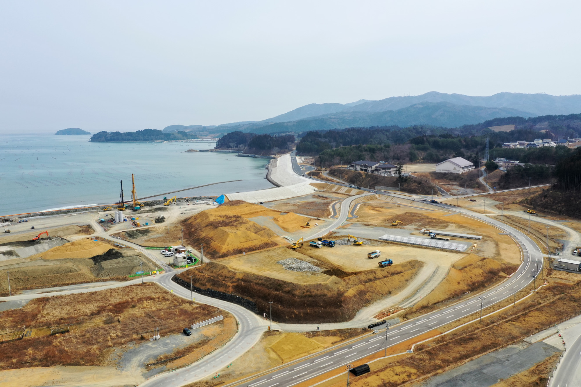 海岸沿いの工事現場で、整備中の道路や建物の基礎部分が確認でき、周囲には重機や資材が配置されている開発中の海辺の写真