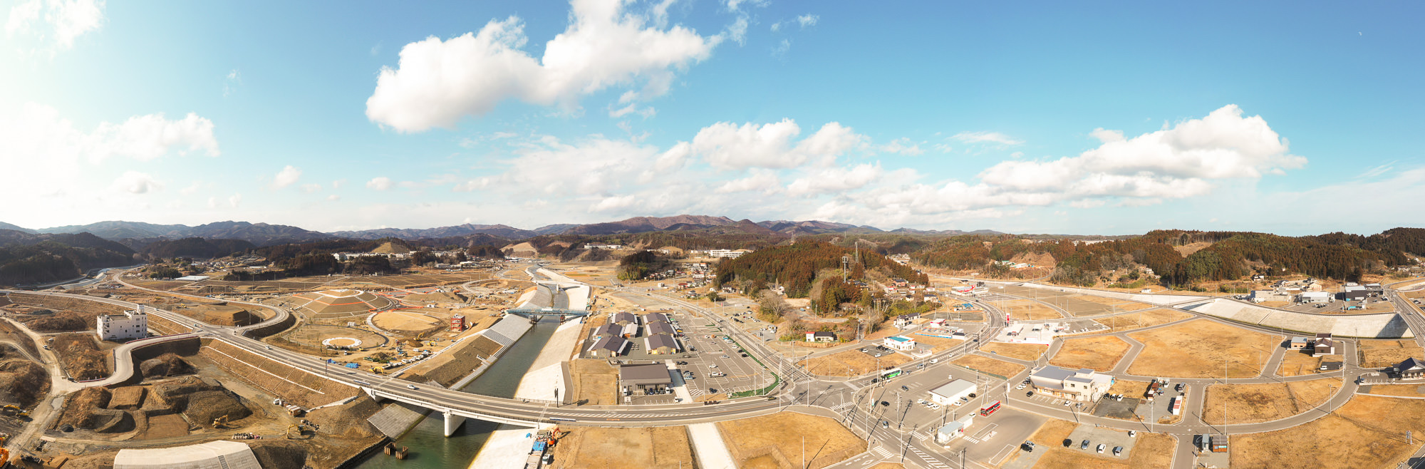 広い範囲にわたる田舎の風景を空から撮影した写真で、川が流れ、その上に橋が架かり、周囲には道路や建物が点在している写真