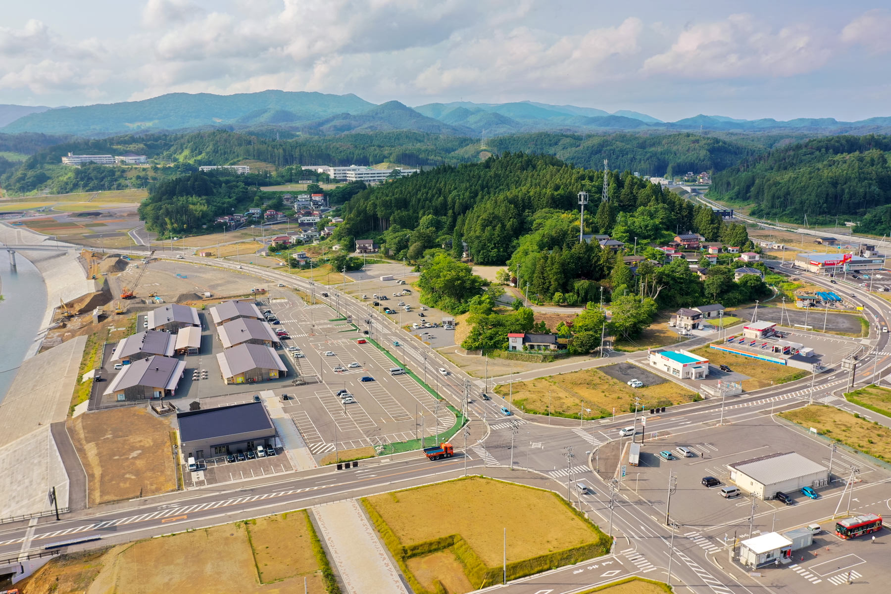 右側には緑豊かな山々、整然とした道路や駐車場、複数の建物が広がっており、町のインフラが整備されている様子がわかる空から見下ろした風景写真