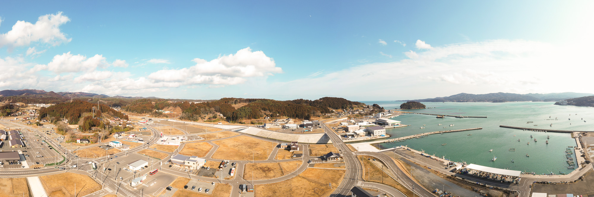 海に面した町の全景を空から撮影した写真で、道路や建物が広がり、右側には港と青い海が見える写真