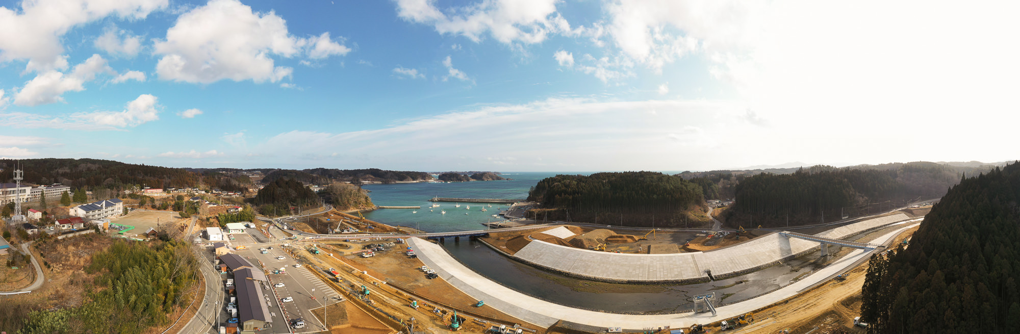 海沿いの町を空から撮影した写真で、建設中の防波堤や道路が広がり、海に面した地域の開発の様子が見える写真