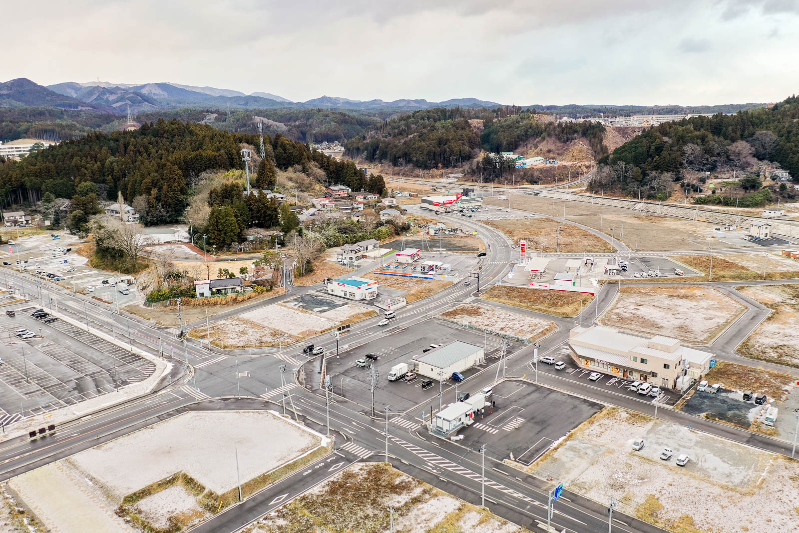 復興が進む広範囲の街並みと再整備された道路が見え、周囲を山に囲まれた小さな町の中心部の昼間の風景を高台から定点カメラで撮影した写真