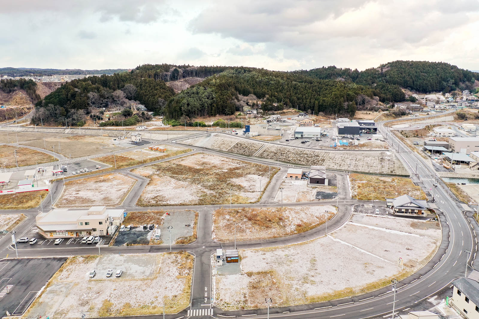 再区画された住宅地が広がり、建物がまばらに建ち始めている様子と、山間の町の昼間の風景を高台から定点カメラで撮影した写真