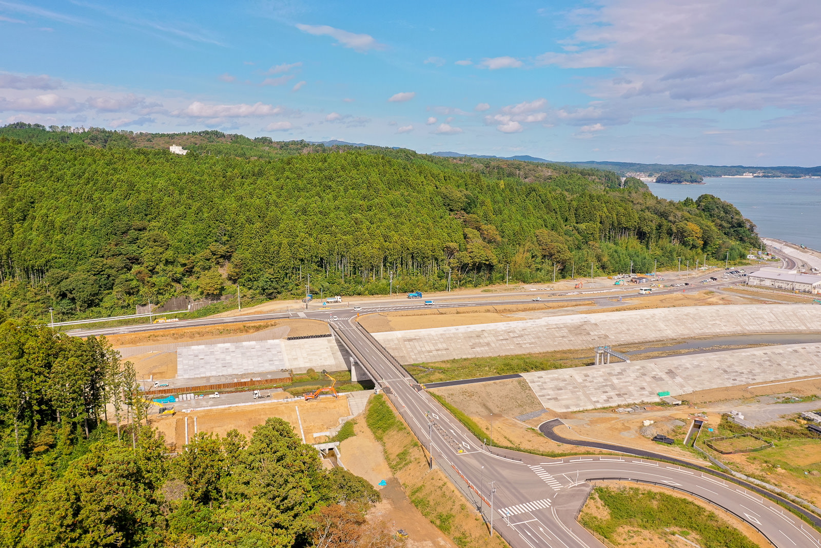 広々とした道路が交差する地点を中心に、周囲には緑豊かな森林と青く広がる海が見渡せる自然に囲まれた交差点の写真