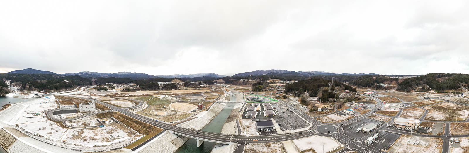 大きく湾曲する川と整備された護岸、いくつもの交差する道路が広がる広大な平地の昼間の風景を高台から定点カメラで撮影した写真