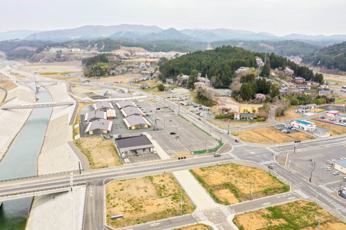 川沿いに建物が並び、その背後には緑豊かな山々が広がっていて、自然と人の暮らしが調和している様子が見える風景の写真