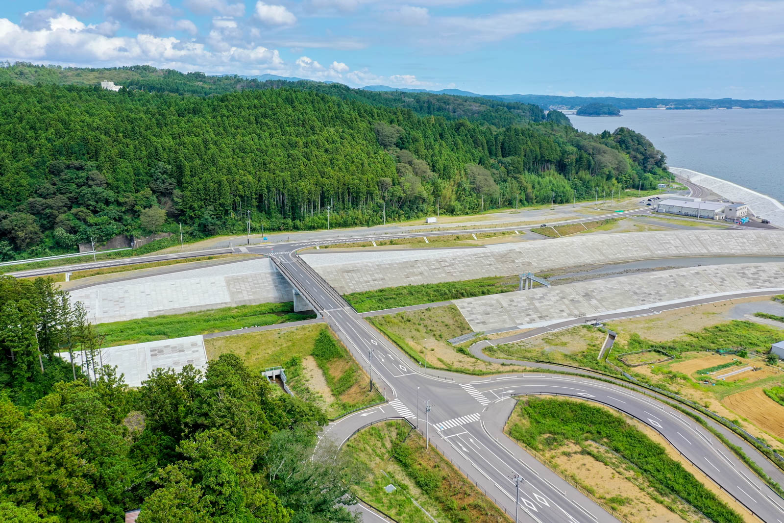 山のふもとを流れる川の両岸に高く築かれた堤防と、それに沿って走る道路、奥に海が見える風景の写真