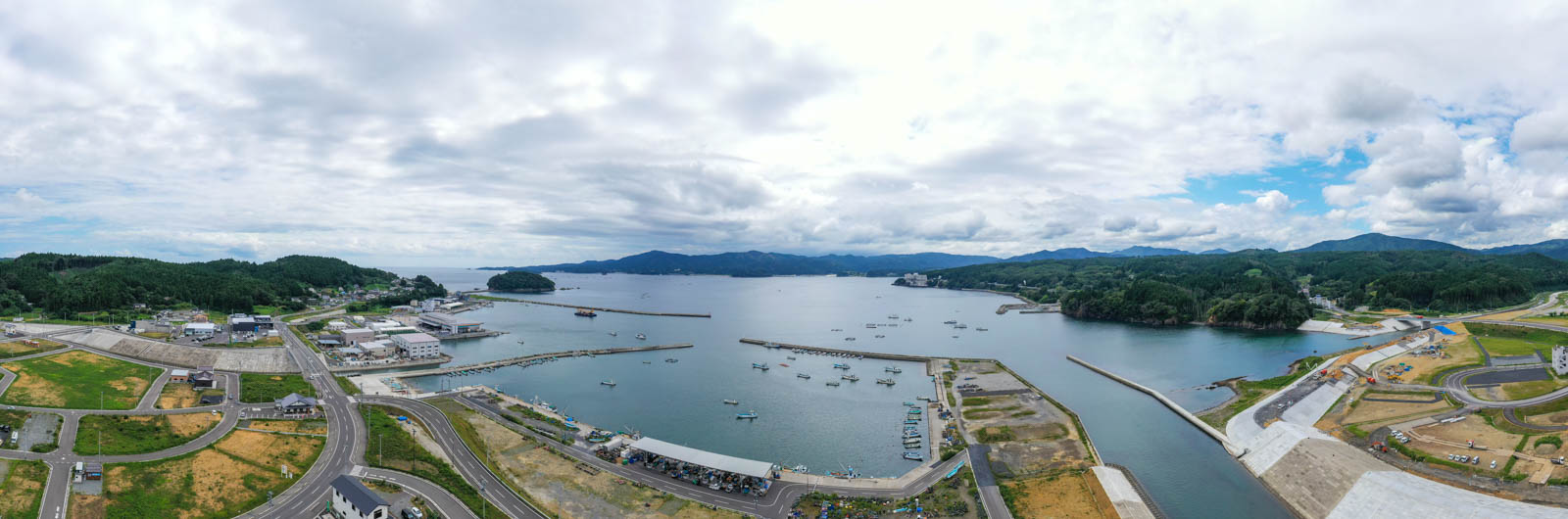 整備された河川と周辺の建物の奥に、港と海、そして多くの漁船が浮かぶ様子を含む広域の風景の写真