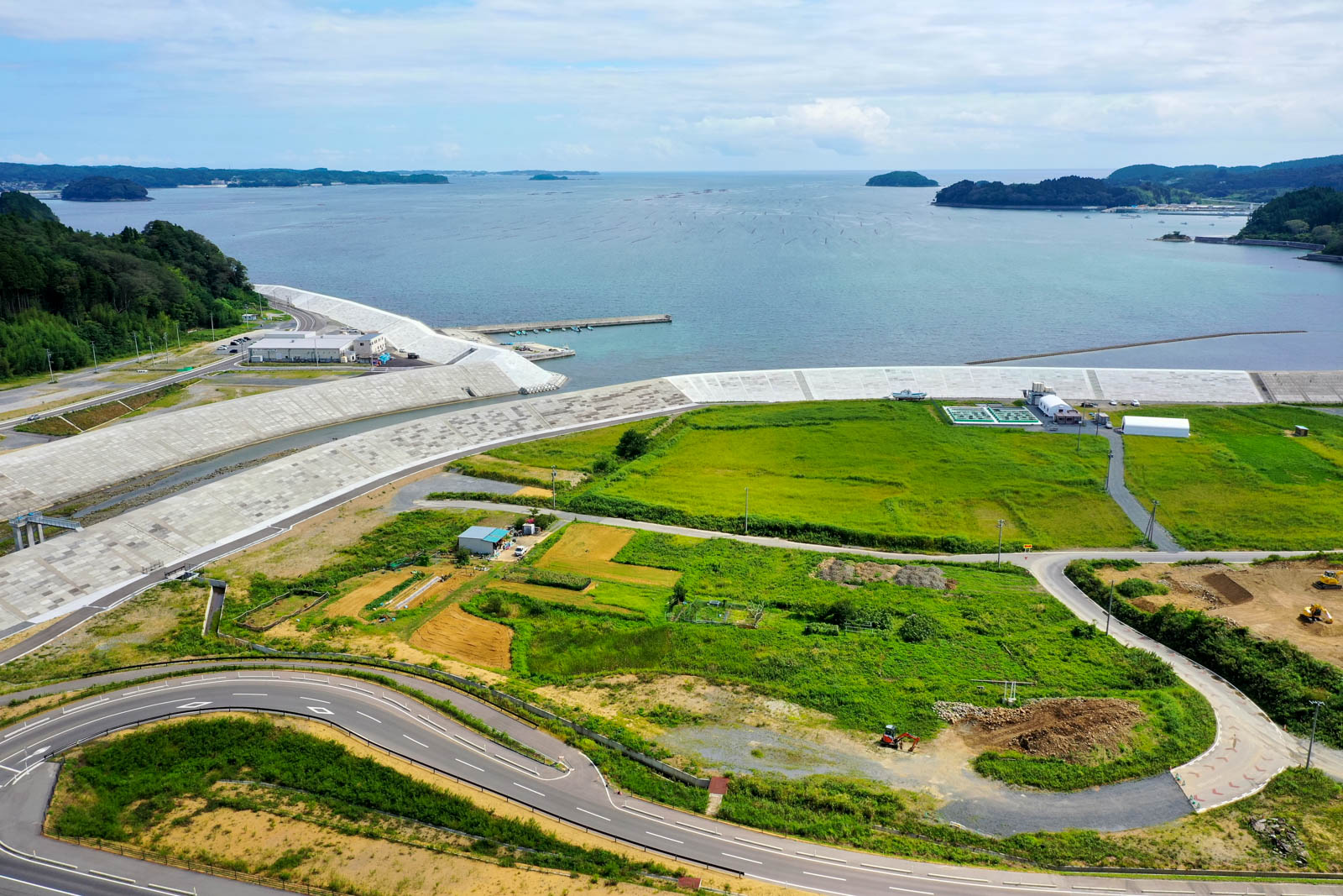 コンクリートで整備された広大な堤防とその奥に広がる湾、堤防の内側には畑や建物が点在する様子を捉えた写真