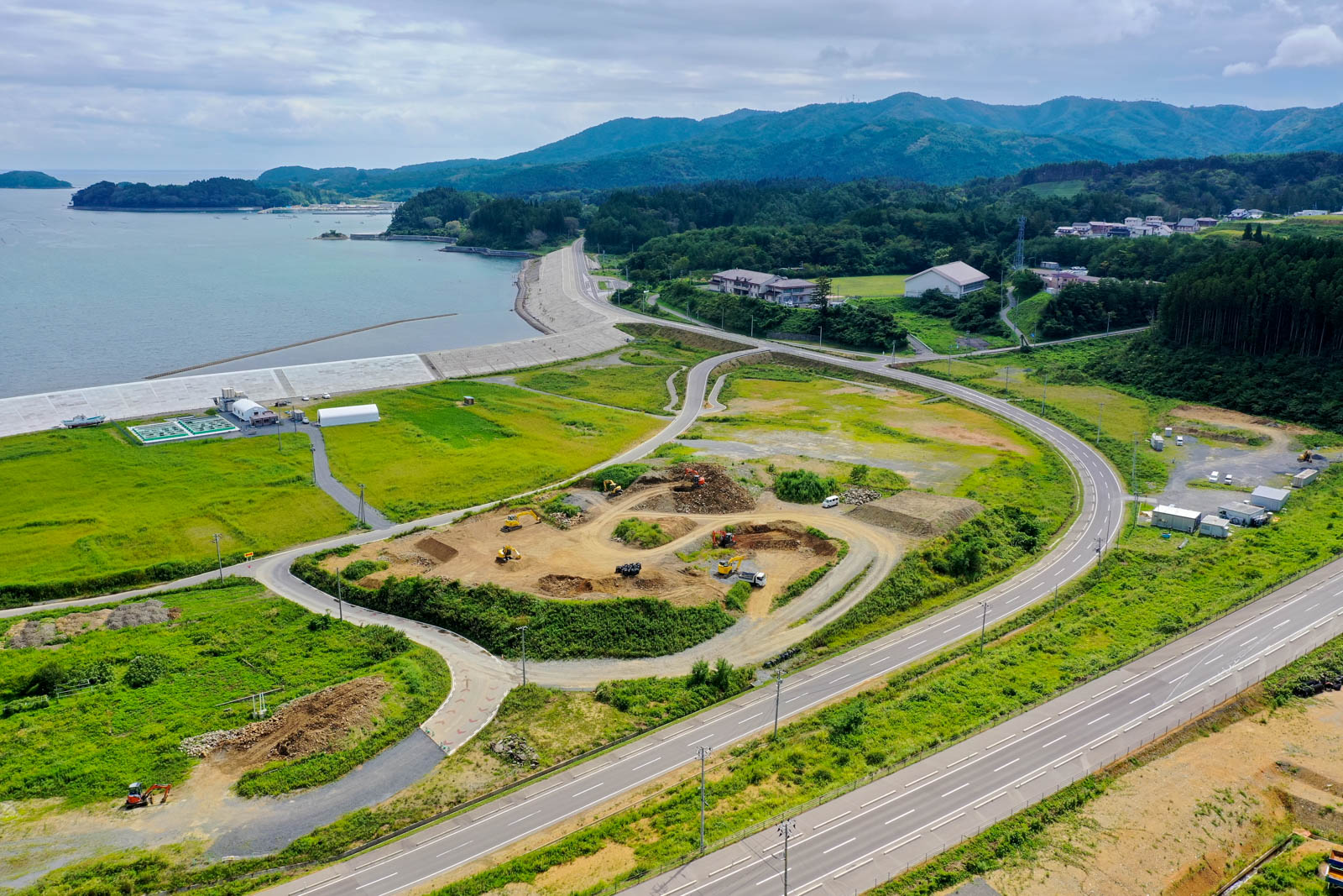 海に面した堤防のすぐそばで、複数の重機が土を掘り起こしている造成工事中の様子を上空から撮影した写真