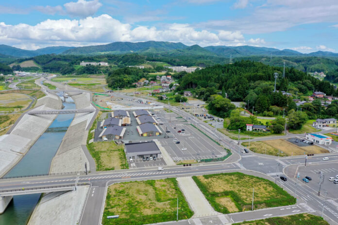川沿いに整備された新しい堤防と広い駐車場、建物が並ぶ様子を上空から見下ろした町の復興地域の写真