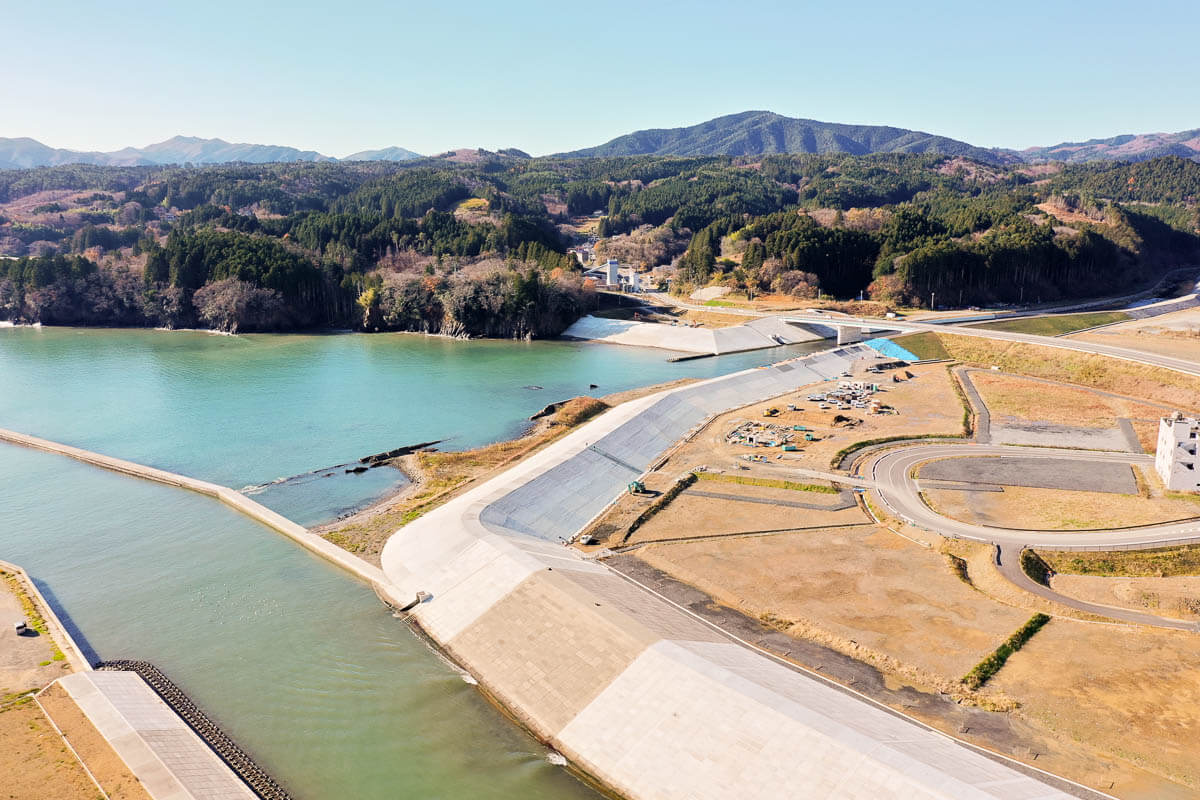 海から川へと続く部分がコンクリート護岸でしっかり覆われており、曲線状の道路と広い更地が見える写真