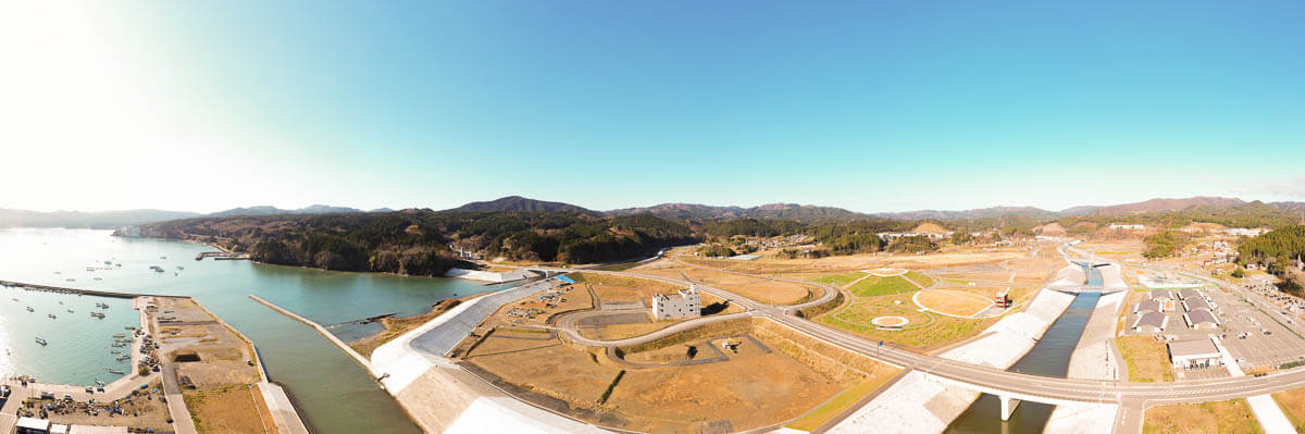 手前の堤防・岸壁は新設され、津波を受け流すような角度で造られていて川沿いの高い護岸と新しい道路網が整備されている写真