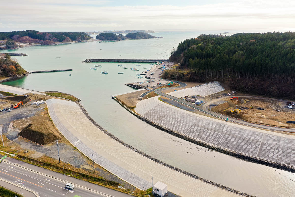 幅広く高いコンクリート護岸が曲線状に整備され山裾を利用した道路整備も進行している様子を写した写真