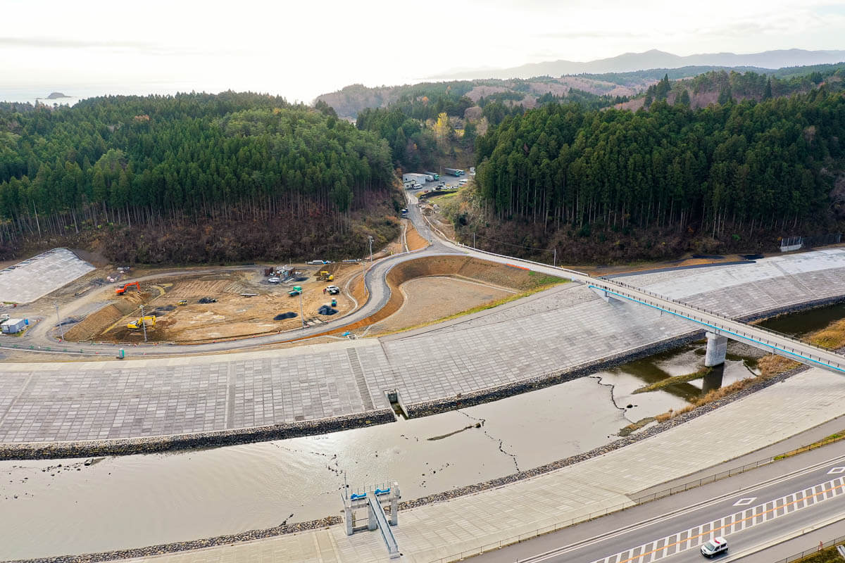 河川と海が合流する場所に高い護岸が築かれ排水ゲートのような構造物があり、河川水を調整しながら外洋との水位差を管理している様子を写した写真