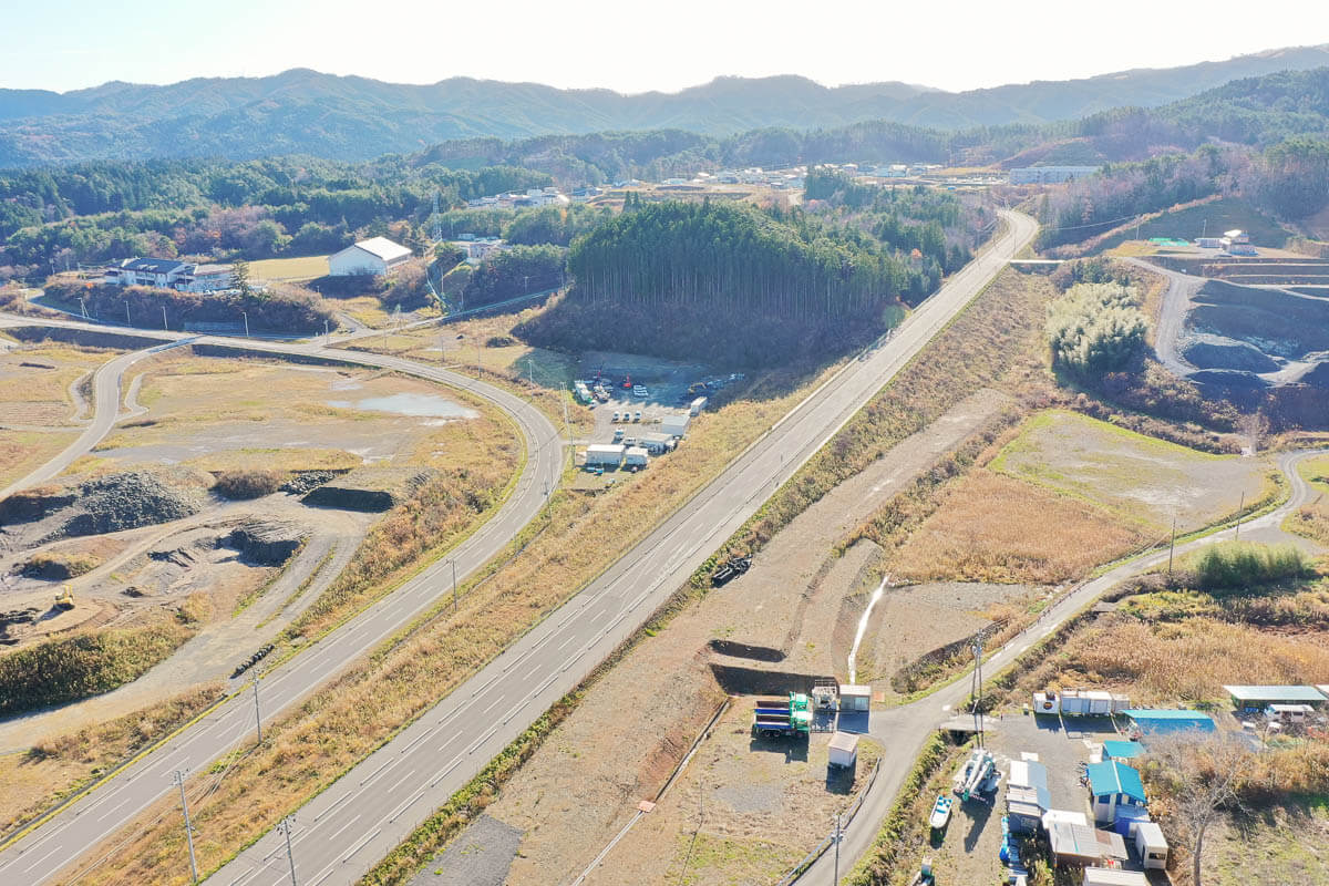 手前には整備された道路が2本平行して伸びていて、片方は高台のような築堤の上を走り、その周囲には造成地や盛土の跡が見え、まだ開発途中の区画もある写真