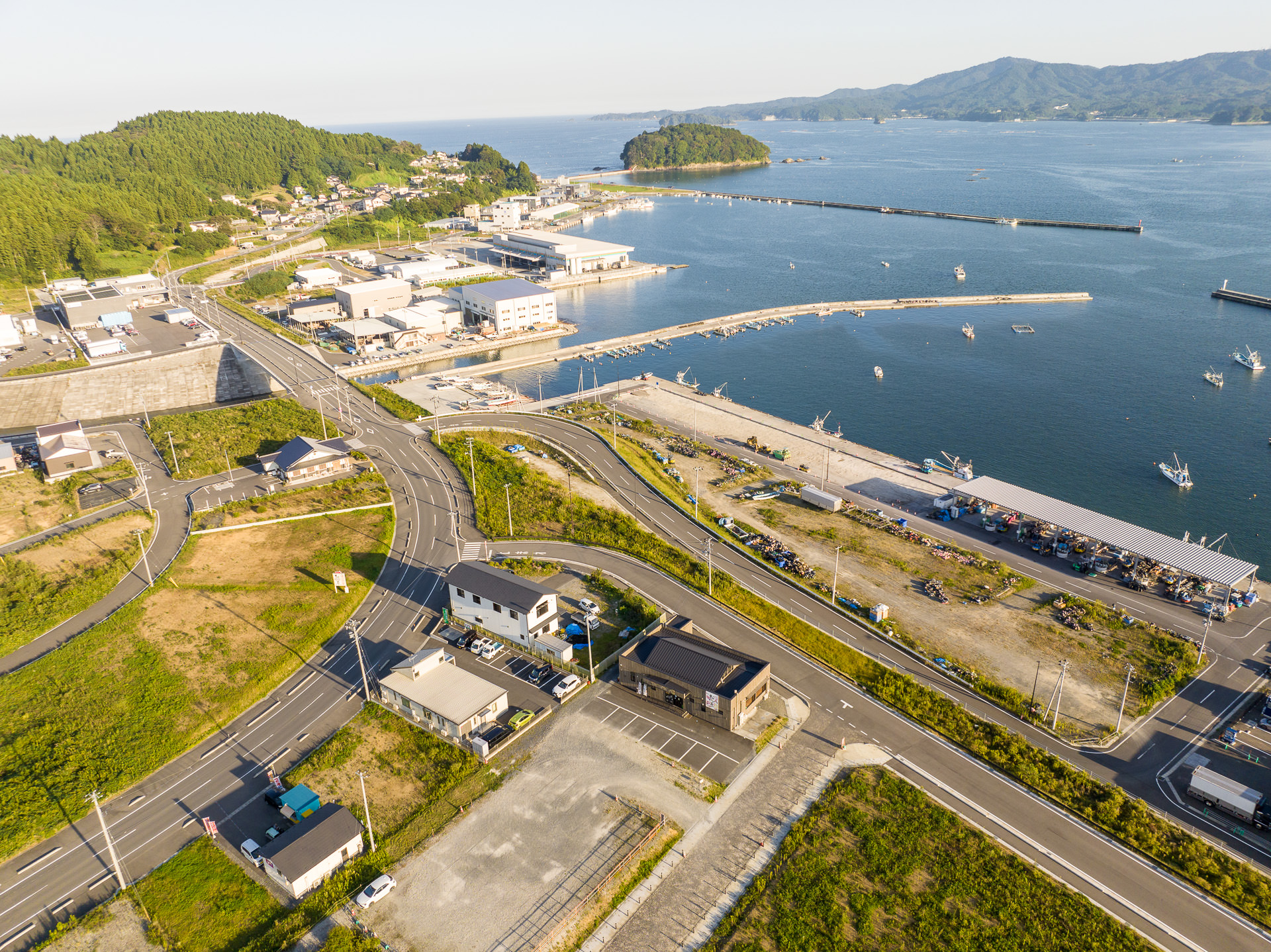 港湾施設や防波堤が整備され、停泊する漁船と陸地の建物群が見える海岸の風景を高台から定点カメラで撮影した写真