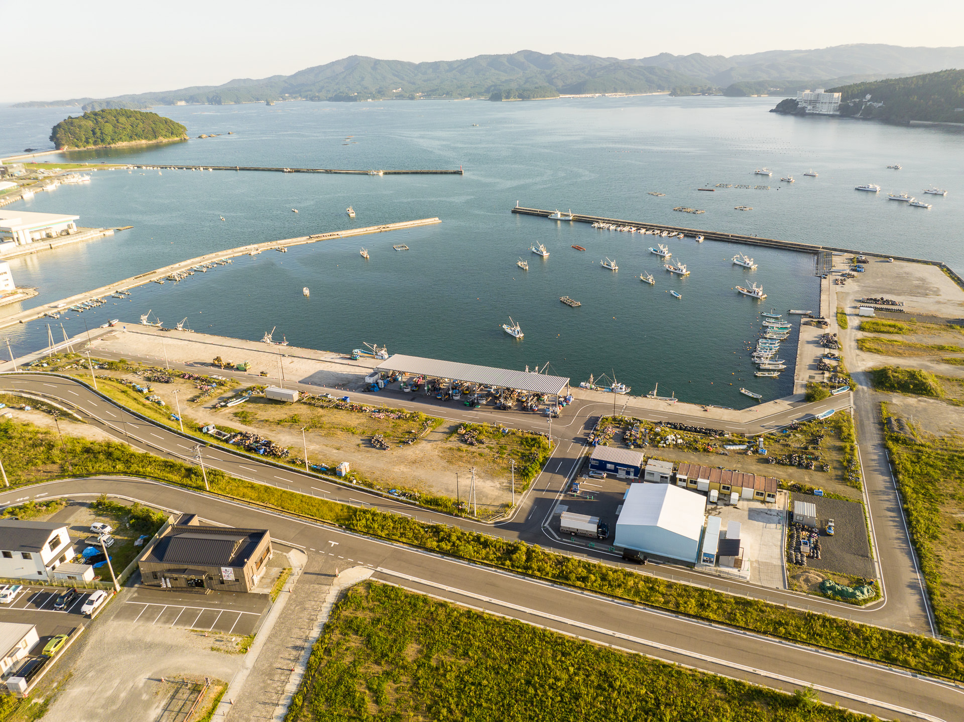 港に停泊する漁船と岸壁、近くの道路や建物が見える海辺の地域の風景を高台から定点カメラで撮影した写真