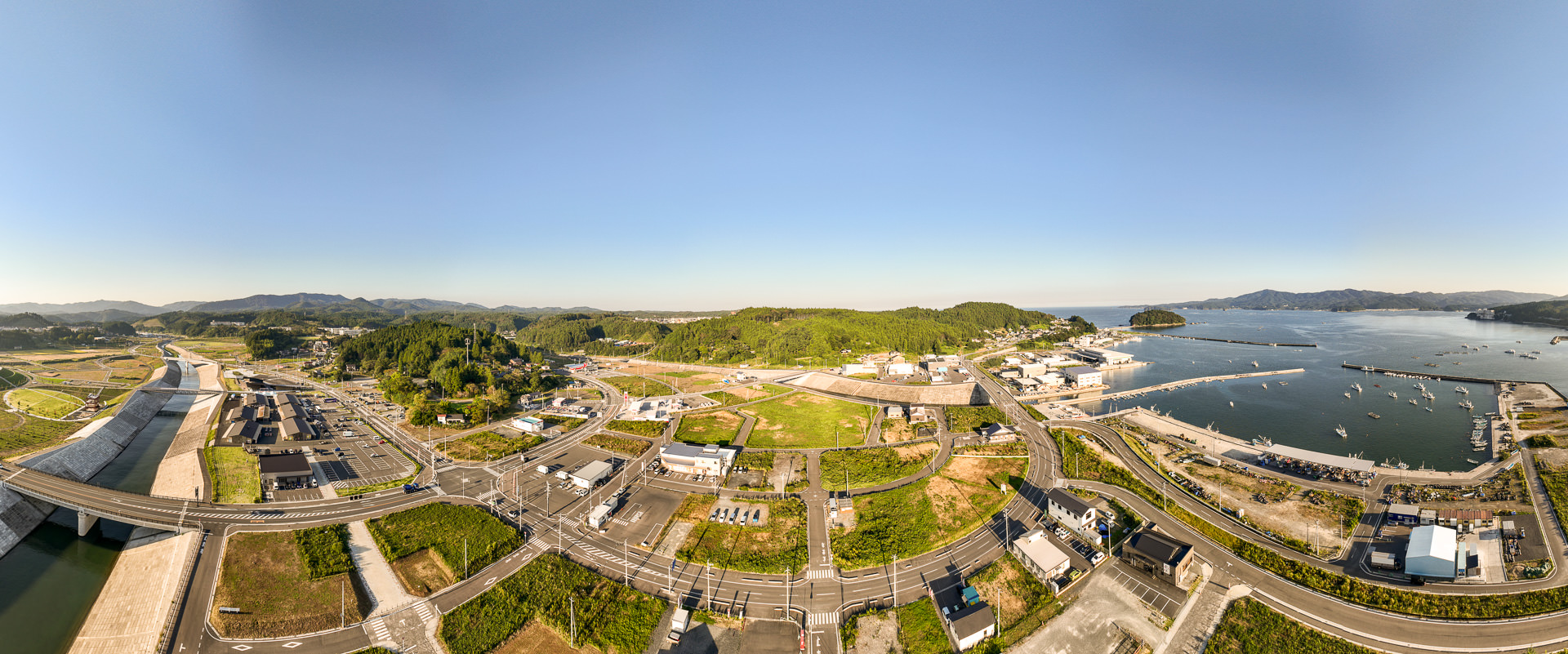 川、橋、道路、港が見渡せ、建物が点在した広い範囲の街並みの昼間の風景を高台から定点カメラで撮影した写真