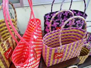 ピンク、紫、黄色などのカラフルなかごバッグがテーブルの上に整然と並べられている室内の写真