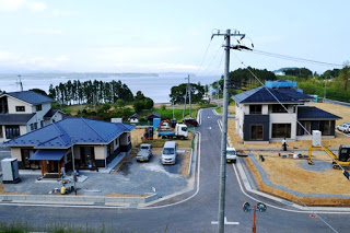 海の近くに位置する住宅地が広がっており、整備された道路や建物が並び、背景には青い海と空が見える様子が写っている写真