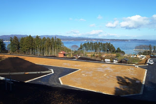 青空の下、土が盛られた造成地の奥に木々と住宅、さらに海と山が広がっている様子が写っている造成地の写真