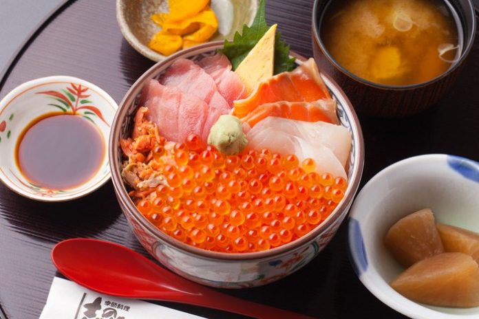 イクラやマグロ、サーモン、白身魚、カニ、玉子焼きなどが美しく盛り付けられた海鮮丼に、味噌汁、漬物、煮物、醤油皿が添えられた南三陸キラキラ丼の定食の写真