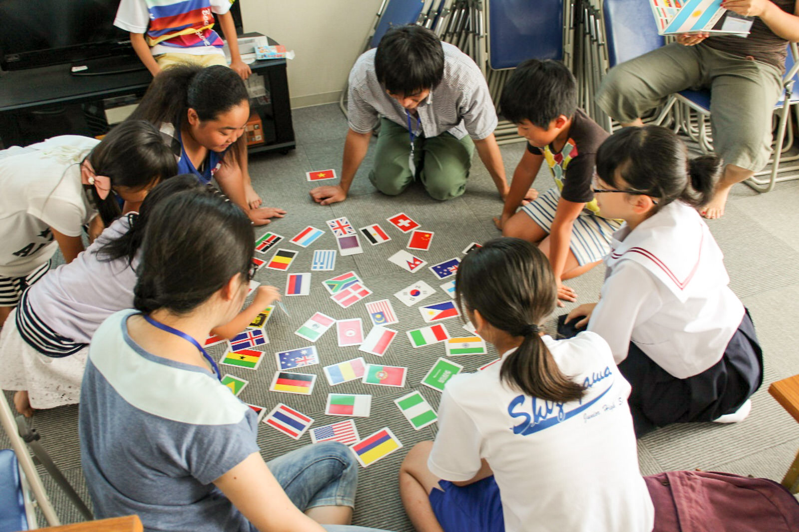 床に円になって座った子どもたちが、中心に置いたさまざまな国旗が描かれたカードを囲んで国旗カルタを楽しんでいる写真