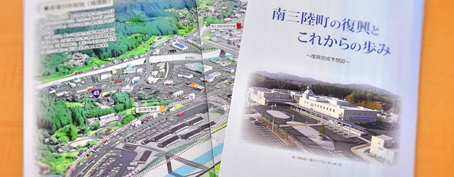 「南三陸町の復興とこれからの歩み」と書かれたタイトルの冊子と、町の復興想像図が載ったページを開いた状態の写真