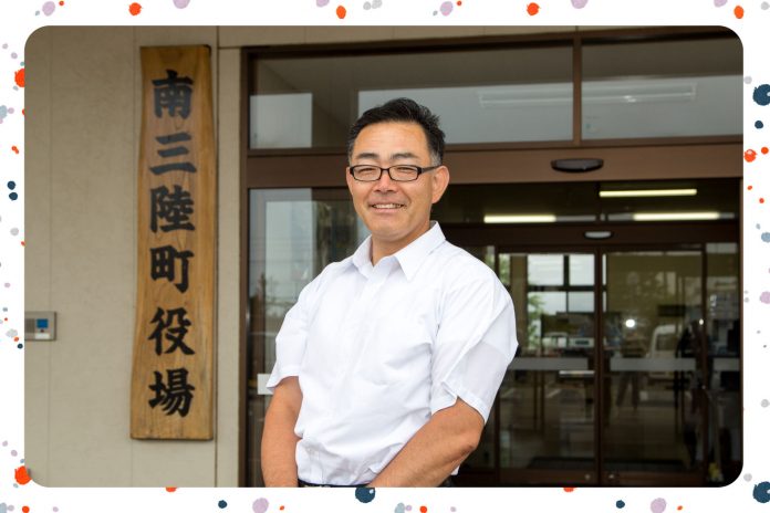南三陸町役場と書かれた木の看板が設置された建物の入り口前で、白いシャツを着た高橋さんが立っている写真にカラフルな縁取りがされている画像