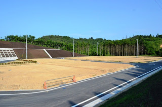 舗装された道路の両側に空き地が広がり、背景には森林が広がっている造成地の写真