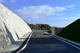 青空の下、両側にコンクリートの擁壁がそびえ立つ坂道が伸びている造成地内の道路の写真
