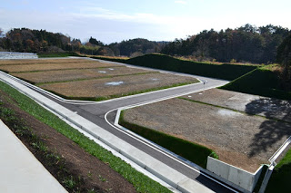 道路で区切られた整地された複数の区画が並び、緑の法面に囲まれた造成地の全景の写真