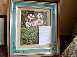 薄いピンク色のナデシコの写真が水色の美しい額に入っており、額の右下にメッセージが書かれたカードが添えられている写真