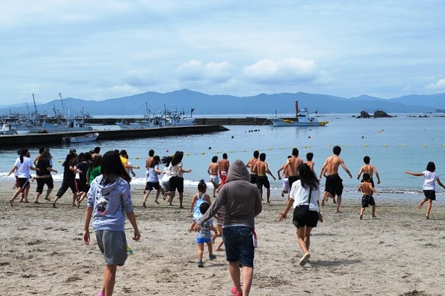砂浜から多くの若者や子どもたちが一斉に海に向かって駆け出していく様子を写した写真
