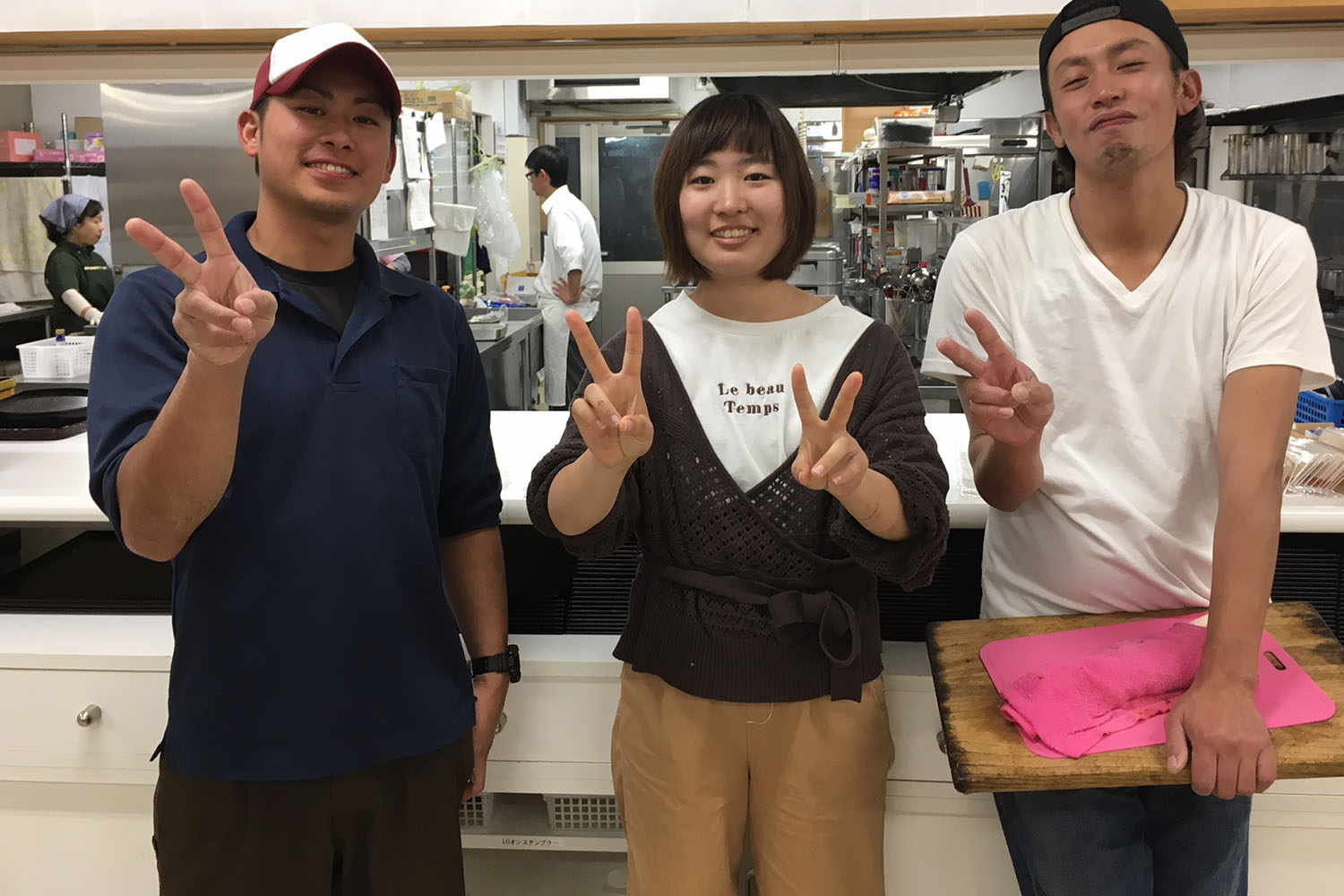 白いTシャツを着た井尻一典さん、紺色のポロシャツを着た高橋真策さん、女性の3人が笑顔でピースサインで撮影している写真