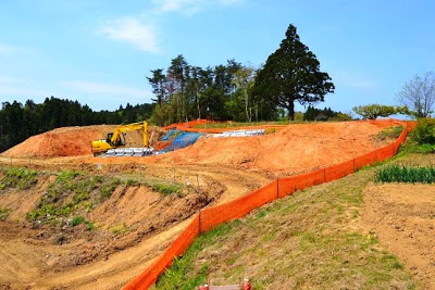 オレンジ色の安全フェンスに囲まれ、黄色い重機が斜面の整地作業をしている造成中の土地の写真