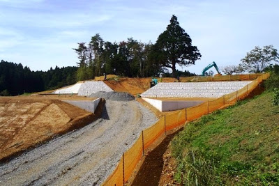 白い擁壁のある斜面に道路が造られており、オレンジ色の安全フェンスが設置されている造成現場の写真