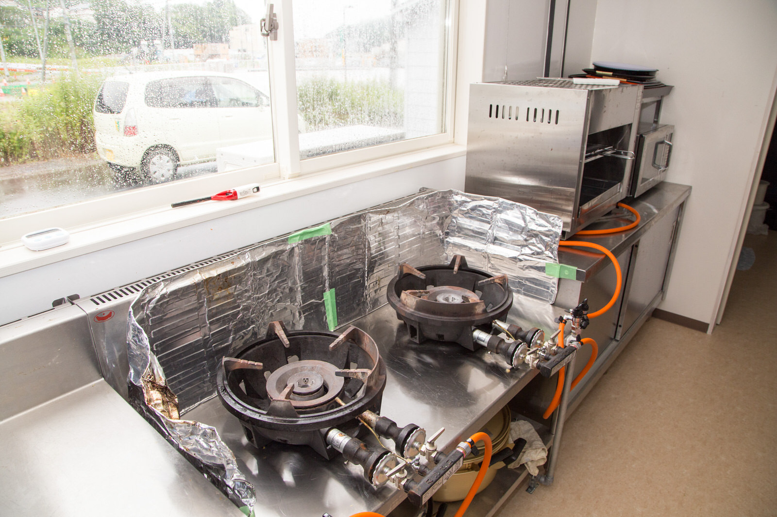 窓際の作業台に二口の業務用のガスコンロと業務用オーブンなどが並んでいる写真