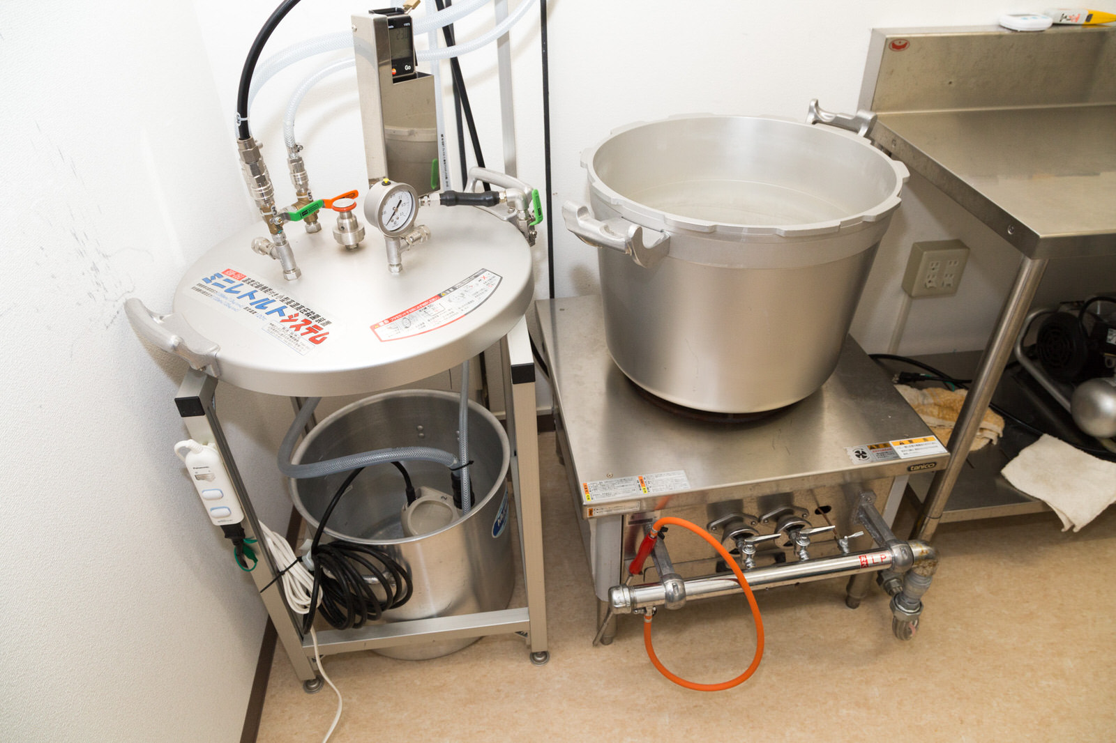 銀色の台に乗った大型鍋と圧力調理器のような機械が並んで設置されている写真