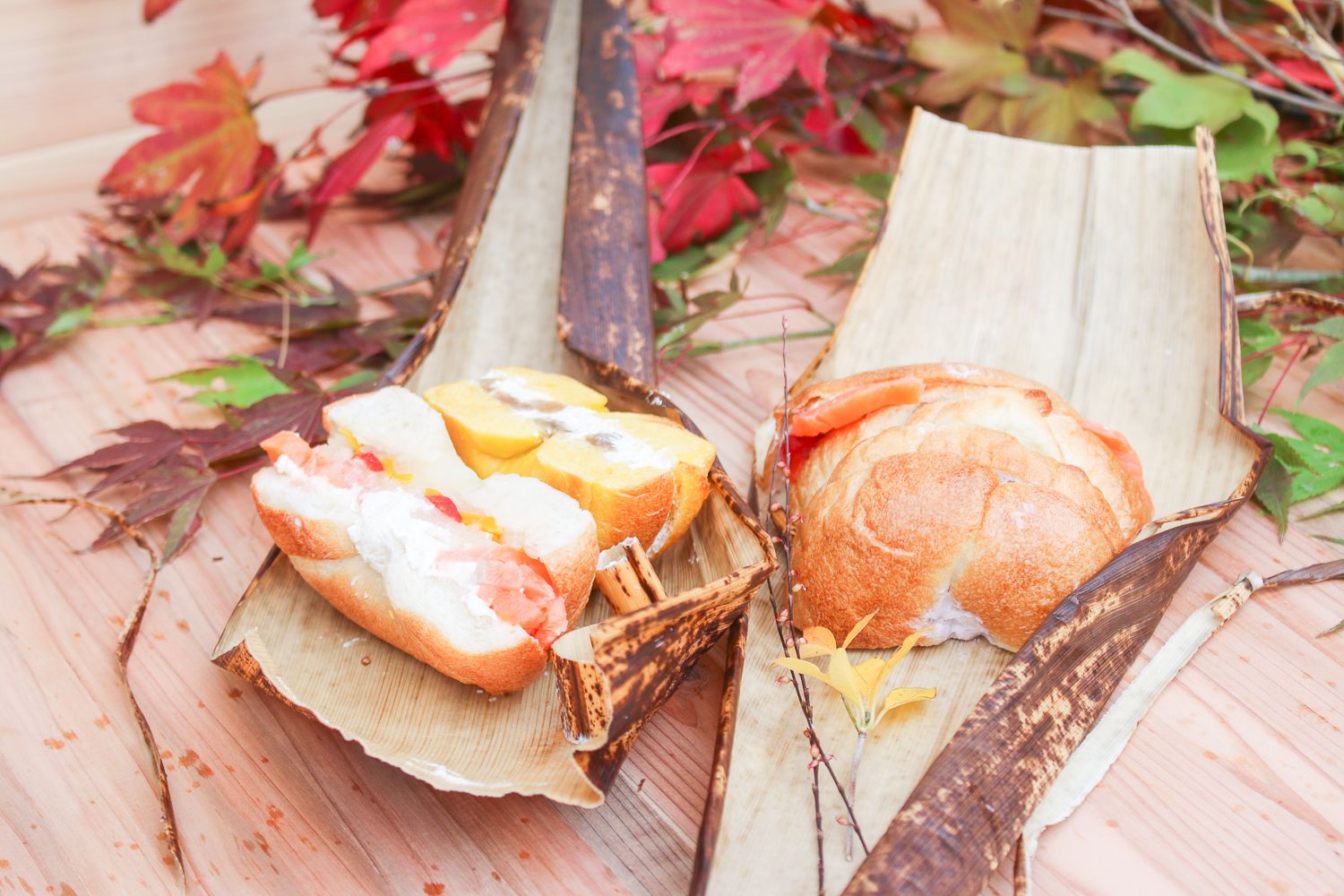 竹の皮の中に、スモークサーモンが挟まった丸いパンの左には中身が見えるように切られて置かれているベーグルサンドのお弁当の写真